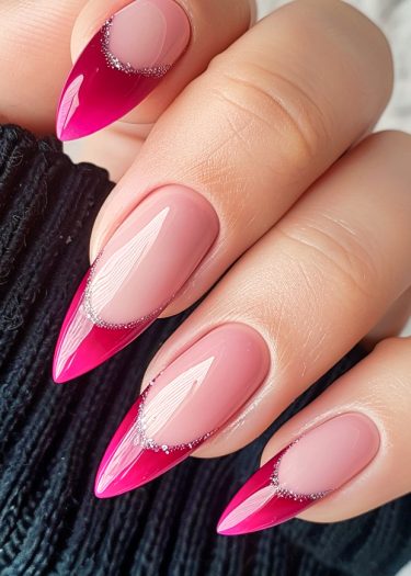 Elegant stiletto nails with pink tips and rhinestones, showcasing a polished manicure against dark fabric.