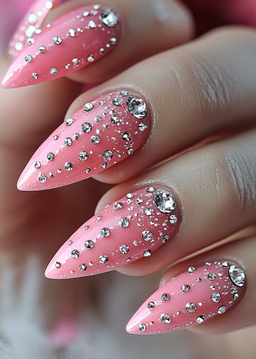 Glamorous pink stiletto nails adorned with sparkling rhinestones for a chic manicure look.