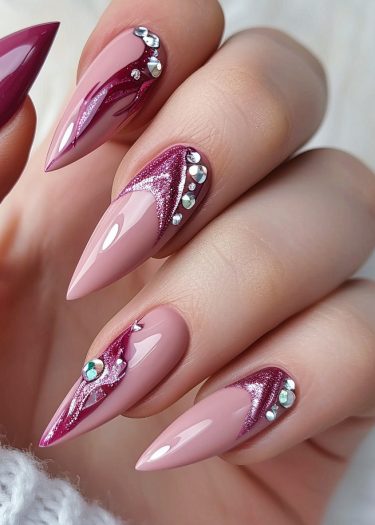 Elegant pink almond-shaped nails with maroon swirls and rhinestones for a glamorous manicure.