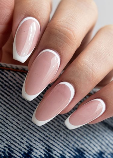 Elegant pink and white nail art design on almond-shaped nails against denim background.