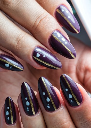 Stunning purple almond nails with black stripes and gold accents showcase elegant nail art design.