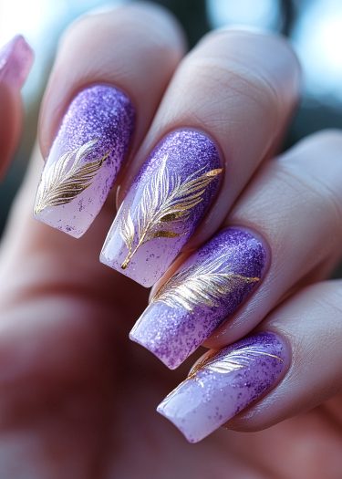 Elegant purple gradient nails with gold feather designs for a luxurious manicure look.