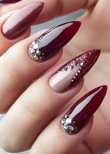 Elegant burgundy almond nails featuring glitter and rhinestones for a luxurious manicure.