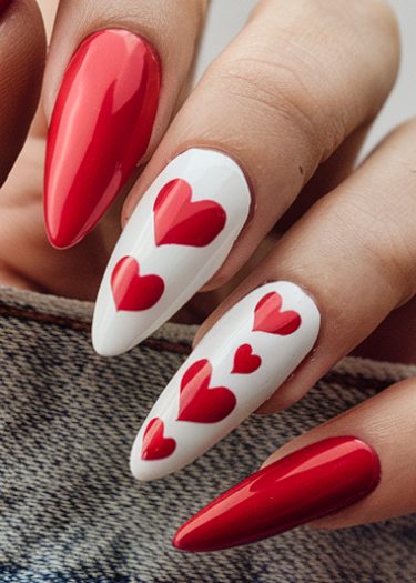 Elegant red and white nail art featuring hearts on almond-shaped nails against a denim background.