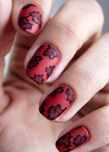 Elegant matte red nails with intricate black lace design showcase sophisticated nail art.