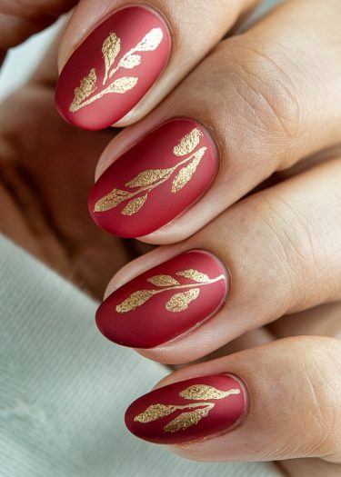 Elegant matte red nail art with gold botanical designs for a chic, sophisticated look.