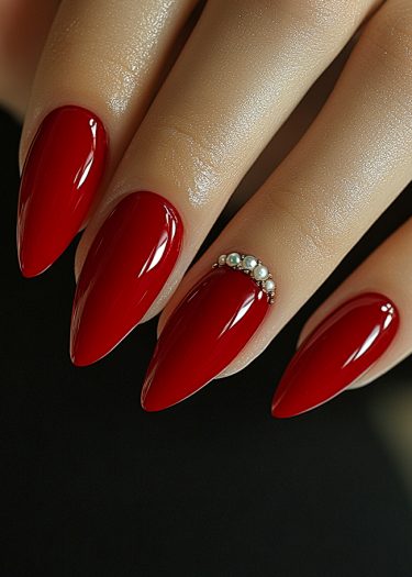 Elegant red stiletto nails with pearls, showcasing luxurious nail art and meticulous manicure details.