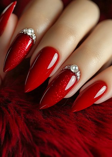 Elegant red nail art with gemstones and pearls on luxurious velvet fabric.