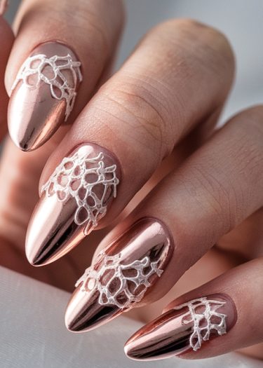 Elegant rose gold chrome nails with intricate white lace design for a luxurious look.