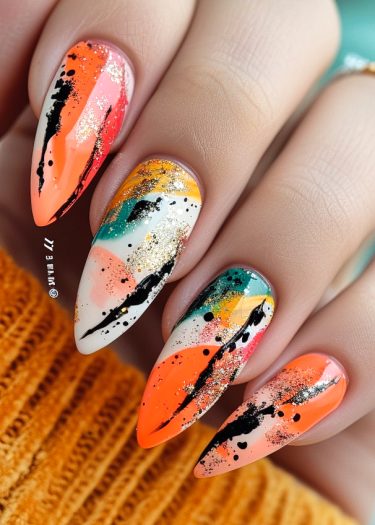 Vibrant stiletto nail art featuring abstract patterns, black splatters, and glamorous gold accents.