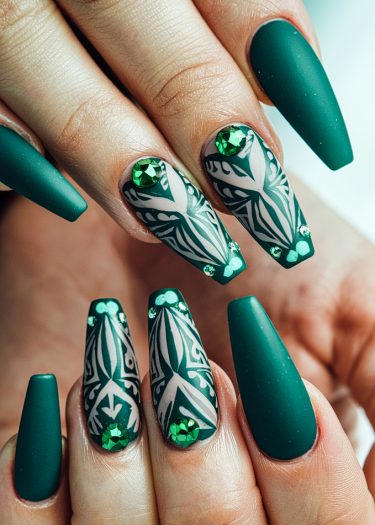 Elegant stiletto nails featuring matte green finishes and intricate tribal designs with rhinestones.