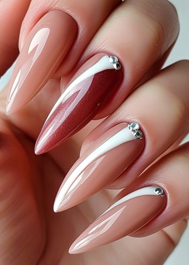 Elegant stiletto nails with burgundy accents, stripes, and rhinestones for a luxurious manicure.