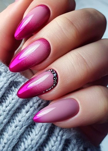 Vibrant pink ombre stiletto nails with rhinestones on a cozy grey background.