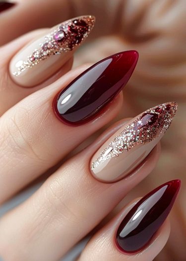 Elegant stiletto nails with burgundy and nude designs, featuring shimmering glitter and jewel embellishments.