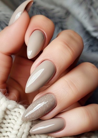 Elegant taupe almond nails with glamorous glitter accent, showcased against a soft textured background.