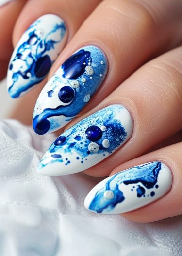 Elegant white and blue nail art with intricate watercolor designs on almond-shaped nails.