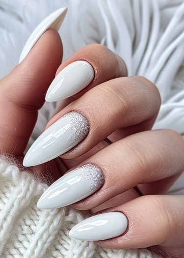 Elegant almond-shaped white nails with glitter gradient, beautifully showcased with a cozy sweater.