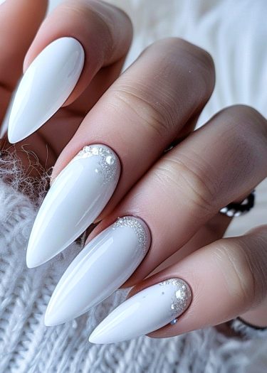 Elegant white stiletto nails with sparkling embellishments for a sophisticated nail art look.