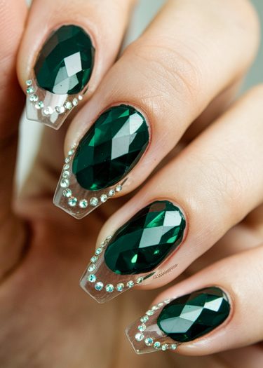 Stunning emerald gemstone nail art with elegant rhinestones on a clear acrylic base.