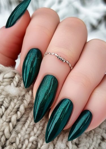 Elegant emerald green stiletto nails with glitter, complemented by a cozy knitted backdrop.