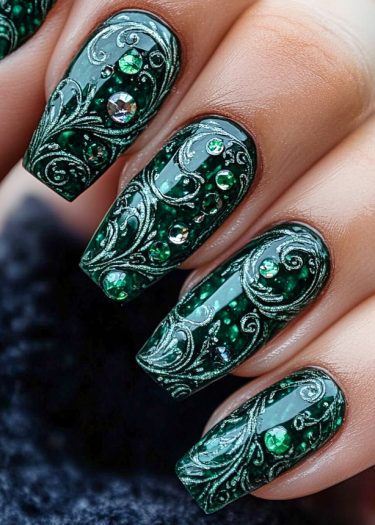 Elegant emerald green nails featuring intricate silver swirls and sparkling gemstones for a luxurious look.