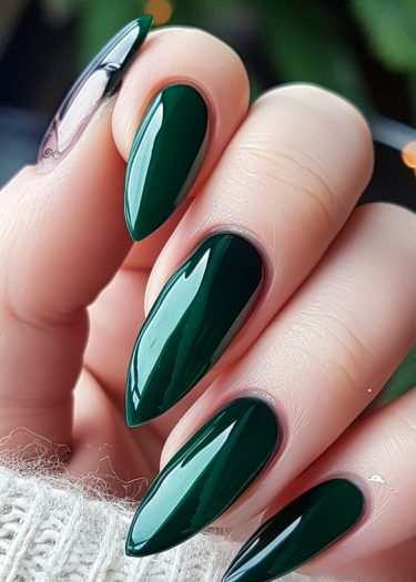 Glossy emerald green stiletto nails on a smooth hand, showcased against a cozy background.