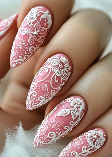 Elegant pink stiletto nails with intricate white floral designs and sparkling gemstones.