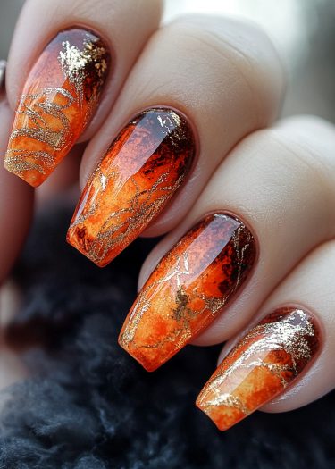 Elegant autumn nails with gold leaf design in warm orange and brown gradient.