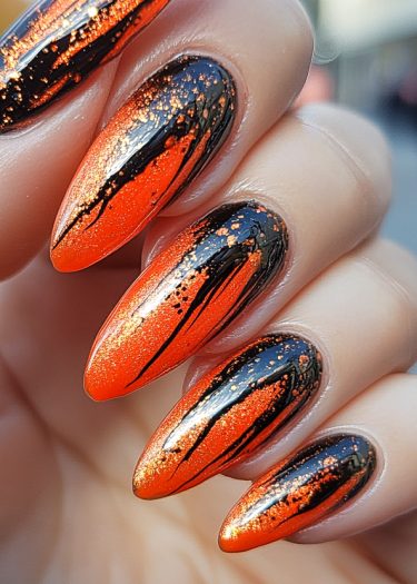 Vibrant orange almond-shaped nails with edgy black abstract art and glitter accents.