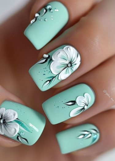 Elegant floral mint manicure with intricate black and white designs and silver accents.