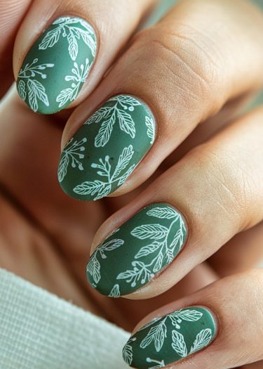 Elegant forest green nail art with white botanical designs on almond-shaped nails.