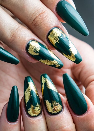 Elegant forest green stiletto nails featuring luxurious gold leaf accents for a stunning look.