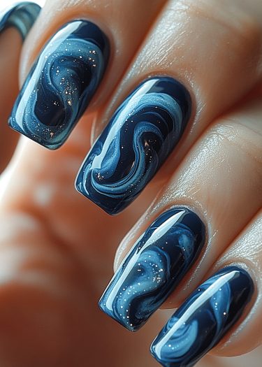 Elegant galaxy nail art design featuring deep blue, swirling patterns and sparkling accents.