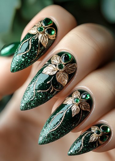 Elegant emerald green stiletto nails with glitter, gold floral designs, and sparkling gemstones.