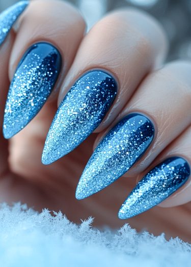 Stunning stiletto nails with navy blue ombre and sparkling glitter on elegant hand.