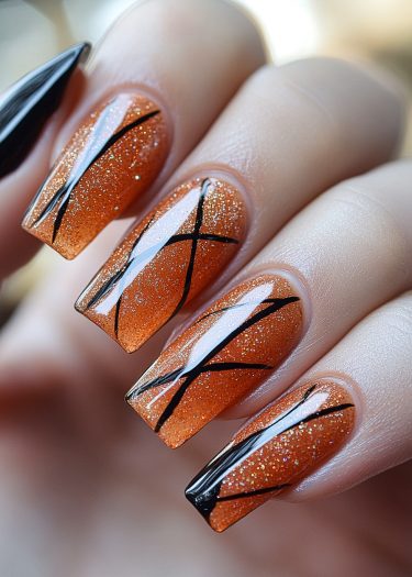 Sparkling burnt orange coffin nails with geometric black designs, perfect for autumnal celebrations.