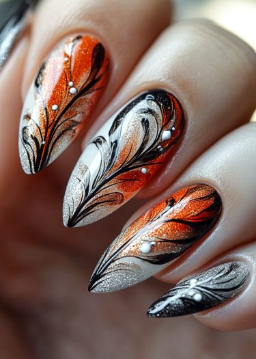 Elegant almond-shaped nails with shimmering orange and silver ombre, featuring black floral designs.