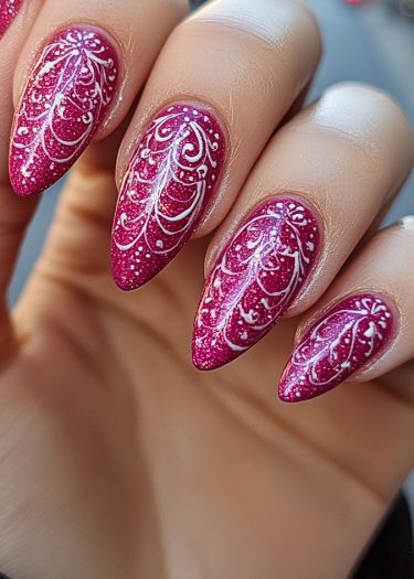 Elegant glittery magenta stiletto nails with intricate white lace patterns for festive occasions.