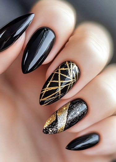 Elegant black almond-shaped nails with gold and silver abstract designs for a luxurious look.