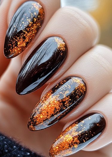 Elegant black nails with vibrant orange glitter create a striking, festive manicure.