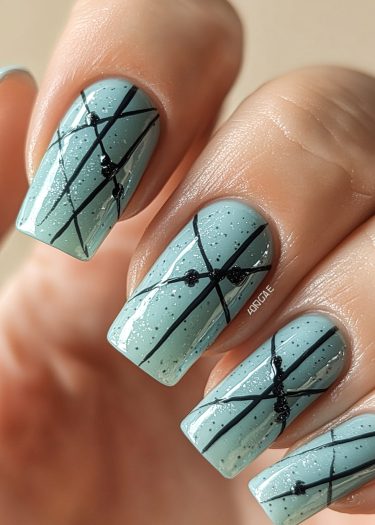 Elegant seafoam green nail art with intricate black designs and shimmering silver glitter.