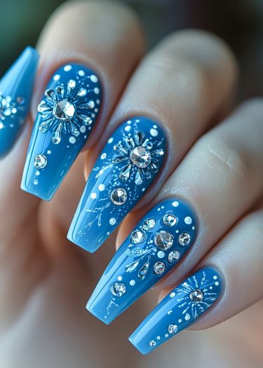 Gorgeous coffin-shaped blue nails with rhinestones and intricate white patterns for stunning nail art.