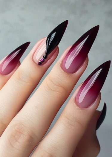 Stunning stiletto nails with burgundy ombré design and glamorous gemstones for chic elegance.