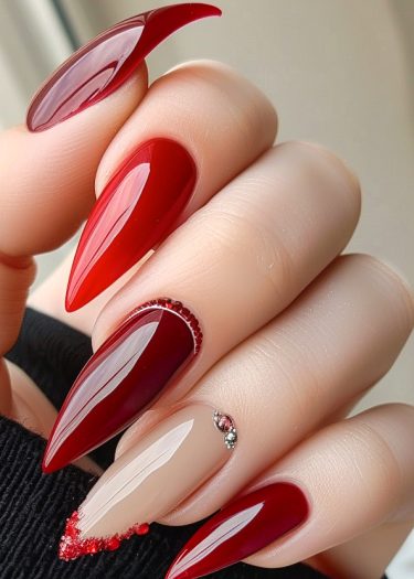 Elegant glossy red almond nails with rhinestones and unique designs for a sophisticated look.