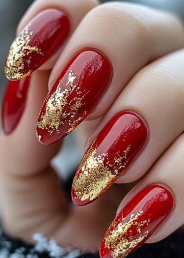 Elegant red almond nails with gold foil design for a luxurious manicure look.