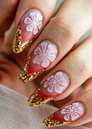 Elegant stiletto nails featuring floral design, glitter tips, and red accents on a soft fabric.