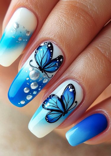 Elegant blue ombre nails featuring intricate butterfly designs and metallic accents.