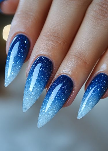 Stunning gradient blue and white glitter stiletto nails with a captivating ombre effect.