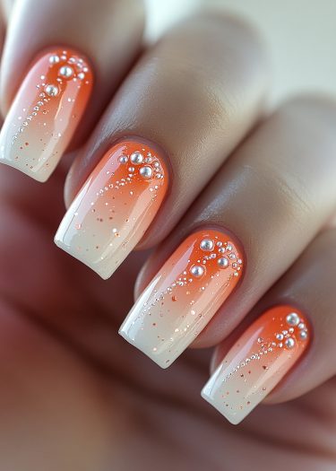 Stylish gradient orange and white manicure with pearl studs and glitter accents.