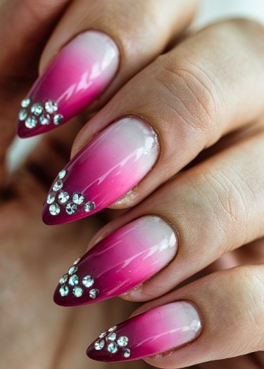 Elegant stiletto nails with a pink-magenta gradient and sparkling rhinestones for a glamorous look.